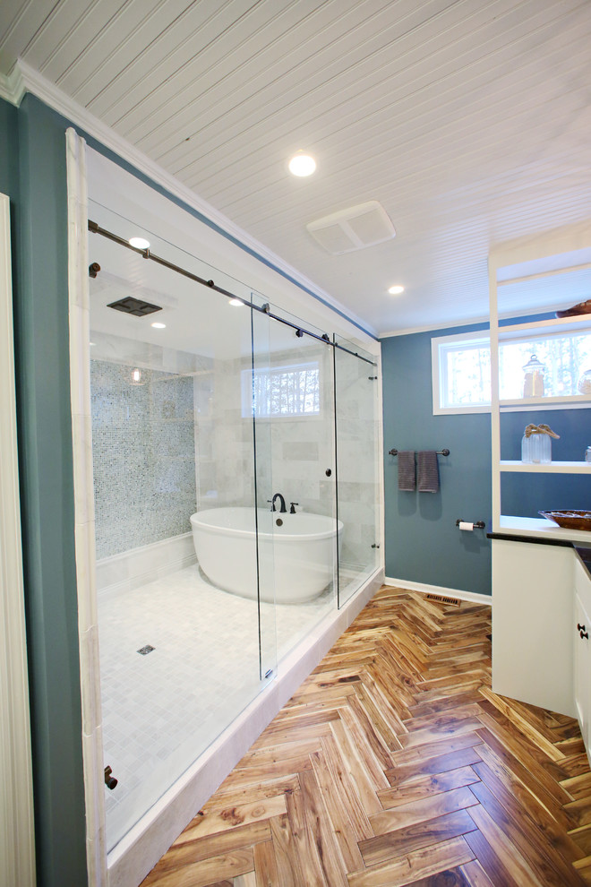Exemple d'une salle de bain principale tendance avec des portes de placard blanches, une baignoire indépendante, une douche ouverte, un mur bleu et un sol en bois brun.