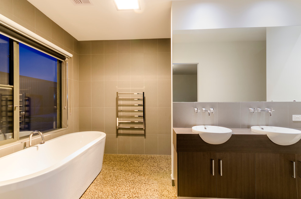 Modern inredning av ett stort en-suite badrum, med ett nedsänkt handfat, skåp i mellenmörkt trä, ett fristående badkar, en öppen dusch, en toalettstol med hel cisternkåpa, grå kakel, keramikplattor, grå väggar och betonggolv