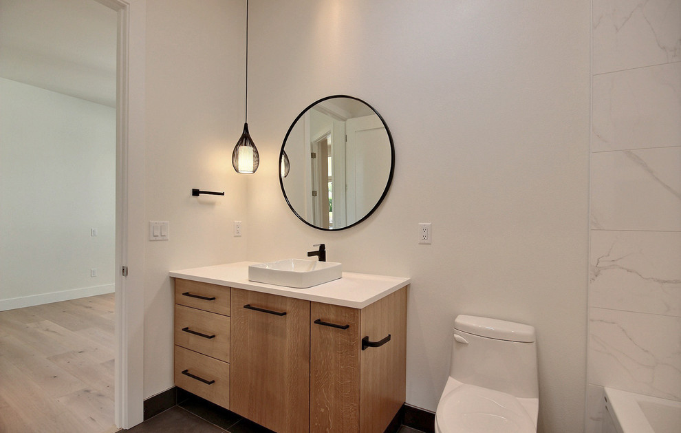 Пример оригинального дизайна: большая детская ванная комната в стиле модернизм с плоскими фасадами, светлыми деревянными фасадами, ванной в нише, душем над ванной, биде, белой плиткой, керамической плиткой, белыми стенами, полом из цементной плитки, настольной раковиной, столешницей из искусственного кварца, серым полом и белой столешницей