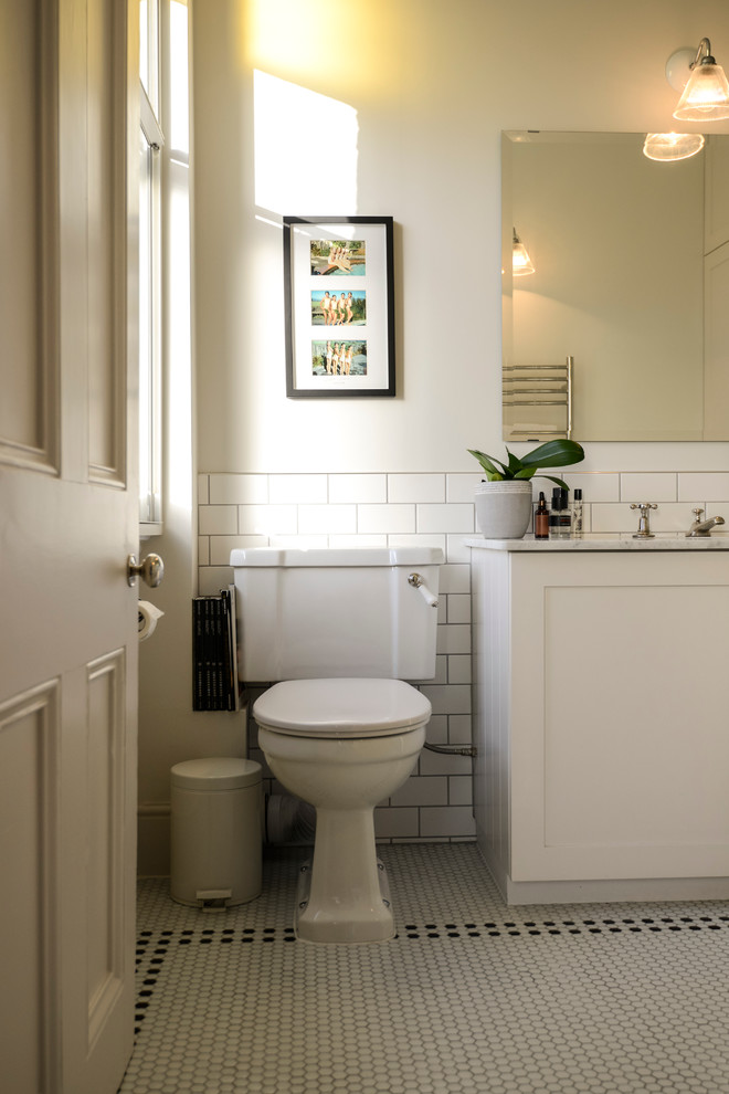 ロンドンにあるお手頃価格のトランジショナルスタイルのおしゃれな浴室 (アンダーカウンター洗面器、分離型トイレ、シェーカースタイル扉のキャビネット、白いキャビネット、大理石の洗面台、白いタイル、サブウェイタイル) の写真