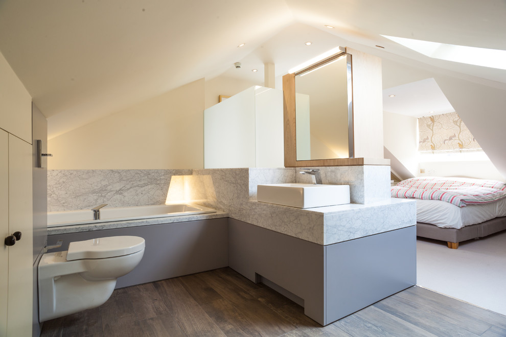 Aménagement d'une salle de bain principale contemporaine avec un placard à porte plane, des portes de placard beiges, une baignoire posée, une douche d'angle, WC suspendus, un mur beige, une vasque, un sol marron et un plan de toilette gris.