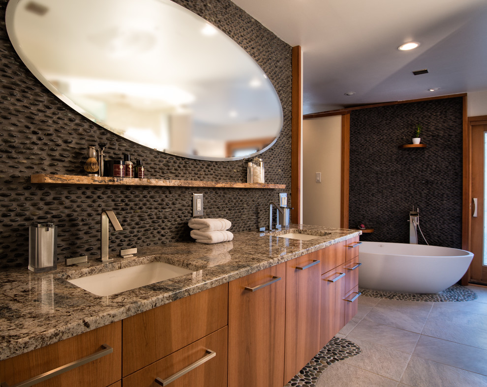 Пример оригинального дизайна: огромная главная ванная комната в стиле модернизм с плоскими фасадами, фасадами цвета дерева среднего тона, отдельно стоящей ванной, черной плиткой, галечной плиткой, столешницей из гранита, открытым душем, врезной раковиной, открытым душем, унитазом-моноблоком, белыми стенами, полом из керамической плитки и серым полом