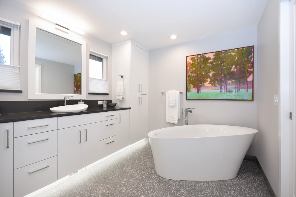 Cette image montre une salle de bain principale design de taille moyenne avec un placard à porte plane, des portes de placard blanches, une baignoire indépendante, un mur blanc, un sol en terrazzo, une vasque, un sol gris, un plan de toilette noir, meuble simple vasque et meuble-lavabo suspendu.