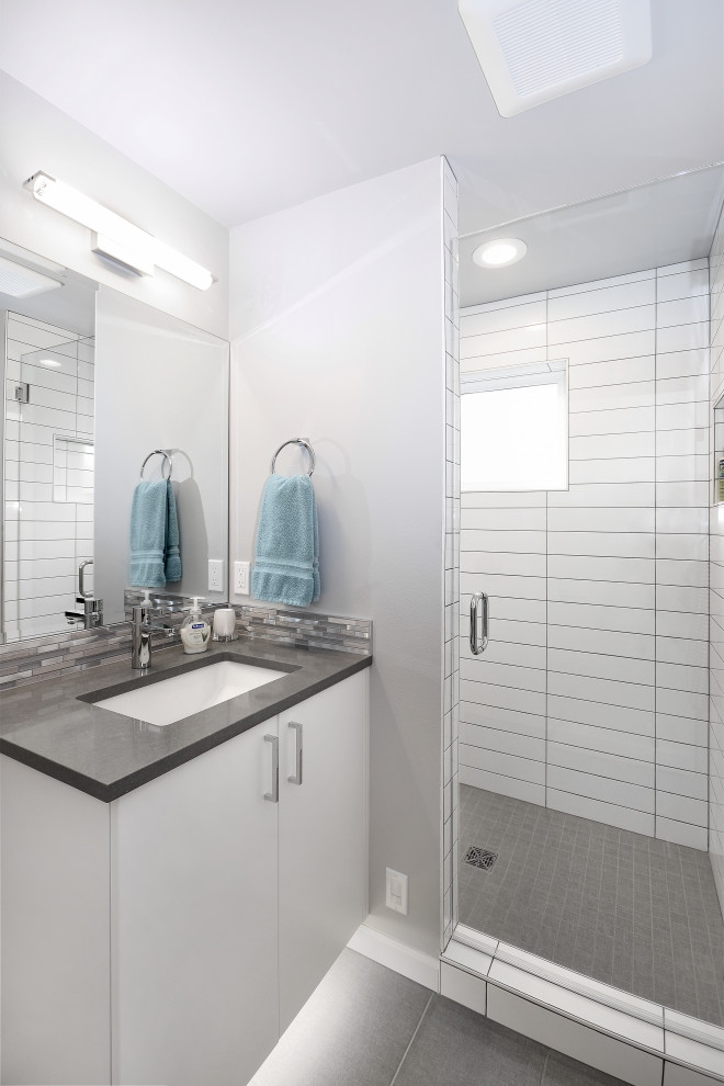 Foto på ett mellanstort funkis grå badrum med dusch, med släta luckor, vita skåp, en dusch i en alkov, vit kakel, grå väggar, klinkergolv i porslin, ett undermonterad handfat, grått golv och dusch med gångjärnsdörr