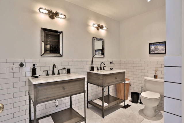 Bild på ett stort industriellt badrum, med möbel-liknande, grå skåp, en toalettstol med separat cisternkåpa, vit kakel, tunnelbanekakel, vita väggar, klinkergolv i porslin, ett undermonterad handfat, marmorbänkskiva och vitt golv