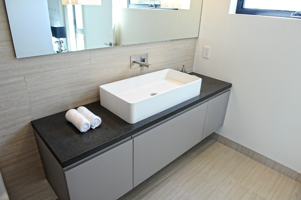 Aménagement d'une grande salle de bain principale contemporaine avec une vasque, un placard à porte plane, des portes de placard grises, un mur gris, un plan de toilette en surface solide, un sol beige et un plan de toilette noir.