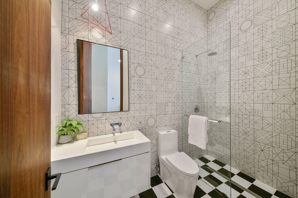 Inredning av ett modernt mellanstort vit vitt en-suite badrum, med ett integrerad handfat, bänkskiva i akrylsten, släta luckor, vita skåp, en hörndusch, en toalettstol med hel cisternkåpa, svart och vit kakel, flerfärgat golv och med dusch som är öppen