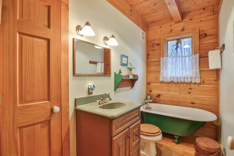 Uriges Badezimmer mit profilierten Schrankfronten, hellbraunen Holzschränken, Löwenfuß-Badewanne, grüner Wandfarbe, braunem Holzboden, integriertem Waschbecken und grüner Waschtischplatte in Raleigh