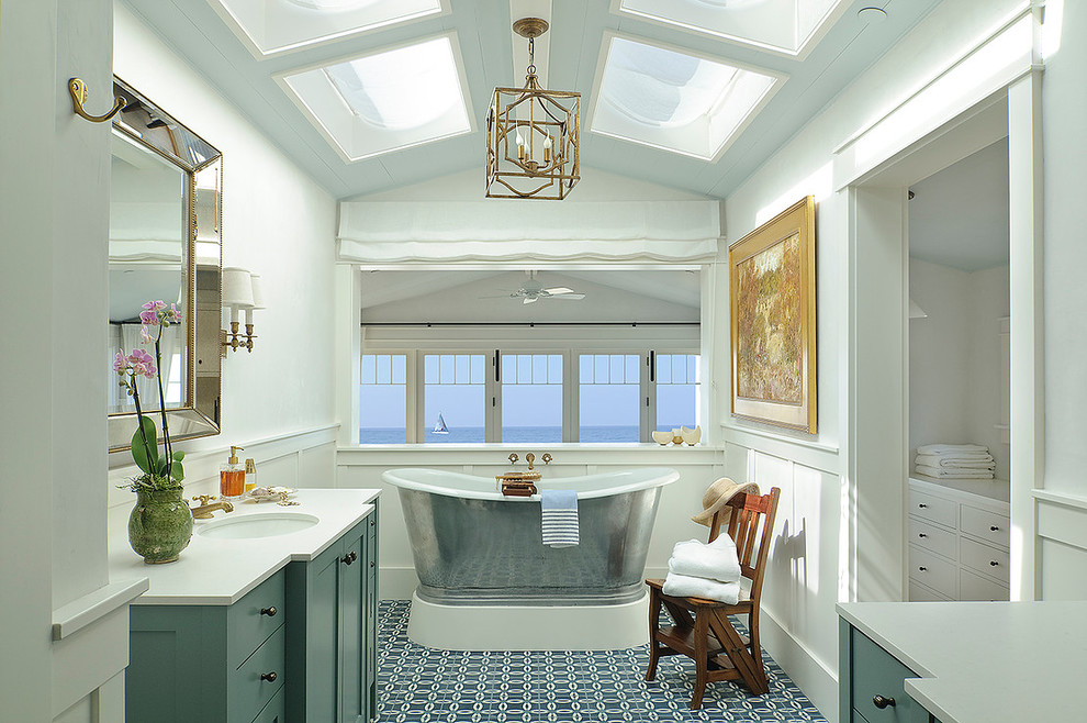 Modelo de cuarto de baño marinero con armarios estilo shaker, puertas de armario verdes, bañera exenta, paredes blancas, suelo de azulejos de cemento, lavabo bajoencimera, suelo azul y encimeras blancas