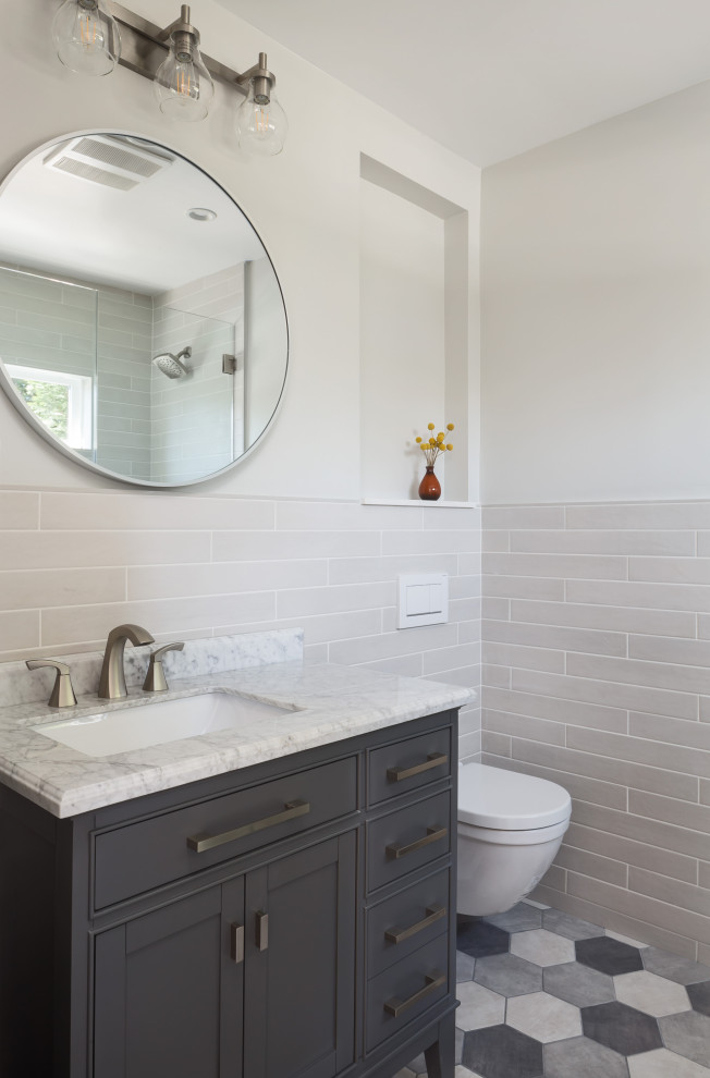 Cette photo montre une petite salle de bain chic avec un placard à porte shaker, des portes de placard grises, WC suspendus, un carrelage beige, des carreaux de porcelaine, un mur gris, un sol en carrelage de porcelaine, un lavabo encastré, un plan de toilette en marbre, un sol gris, une cabine de douche à porte battante, un plan de toilette blanc, une niche, meuble simple vasque et meuble-lavabo sur pied.