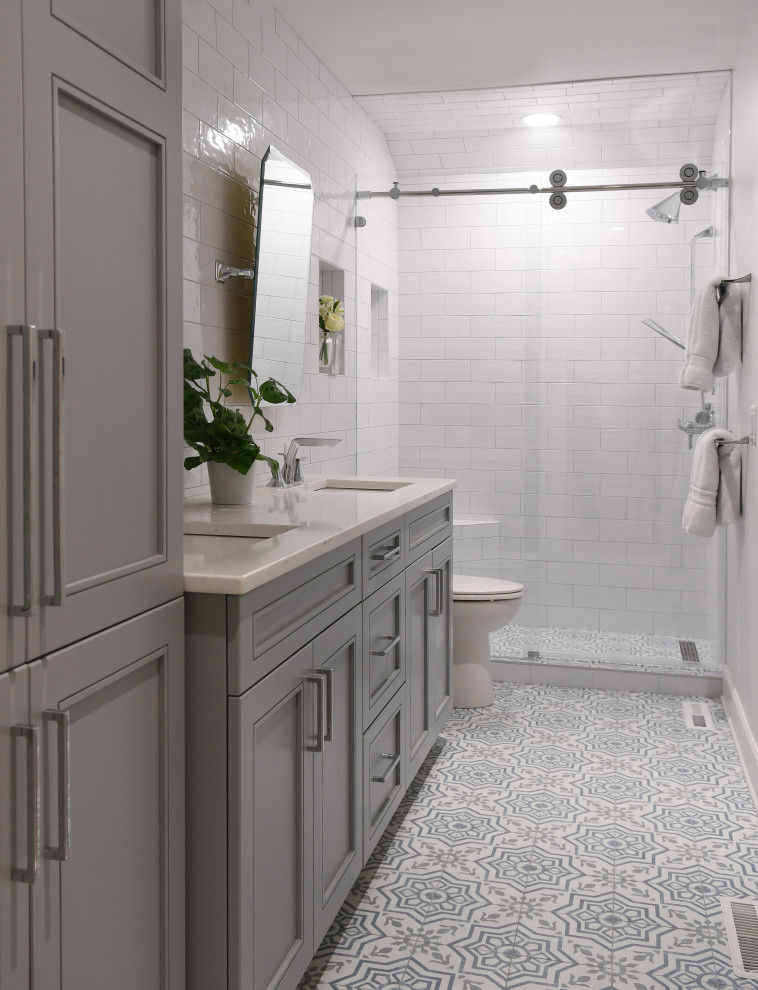 Пример оригинального дизайна: маленькая ванная комната в морском стиле с плоскими фасадами, серыми фасадами, белой плиткой, керамогранитной плиткой, полом из керамогранита, душевой кабиной, врезной раковиной, столешницей из искусственного камня, разноцветным полом, душем с раздвижными дверями, белой столешницей, нишей, тумбой под две раковины и встроенной тумбой для на участке и в саду