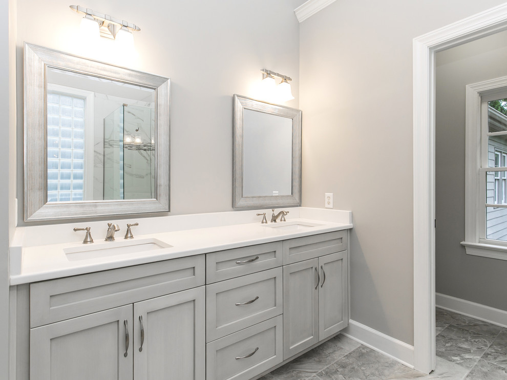 Example of a mid-sized transitional master gray tile, white tile and stone tile porcelain tile and gray floor corner shower design in Raleigh with recessed-panel cabinets, gray cabinets, gray walls, an undermount sink, solid surface countertops and a hinged shower door
