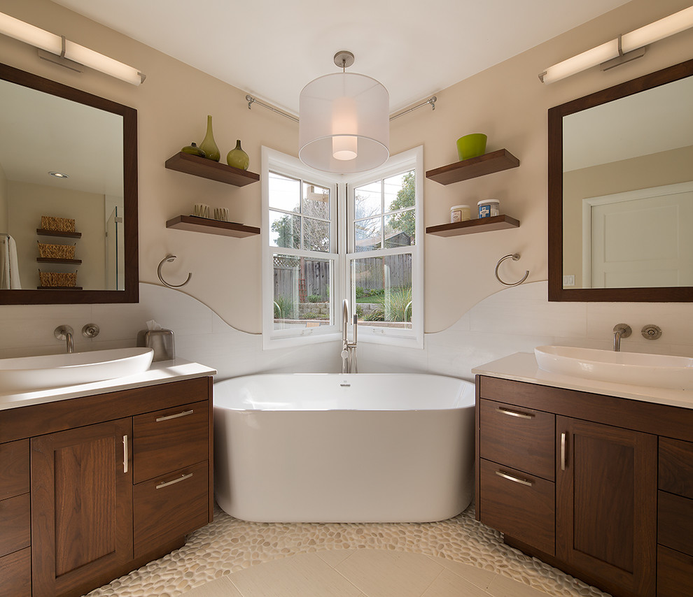 Photo of a traditional ensuite bathroom in San Francisco with a vessel sink, flat-panel cabinets, dark wood cabinets, engineered stone worktops, a freestanding bath, white tiles, porcelain tiles, beige walls and pebble tile flooring.