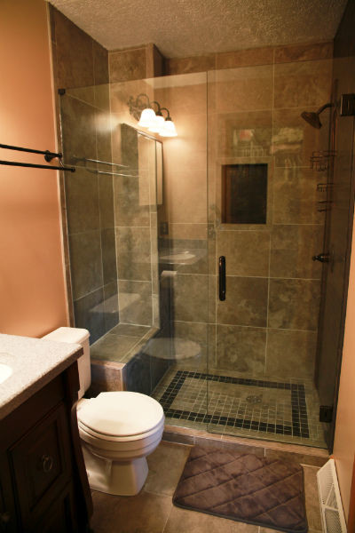 Foto på ett litet vintage badrum med dusch, med luckor med infälld panel, skåp i mörkt trä, en dusch i en alkov, en toalettstol med separat cisternkåpa, grå kakel, skifferkakel, bruna väggar, travertin golv, ett undermonterad handfat, bänkskiva i kalksten, beiget golv och dusch med gångjärnsdörr