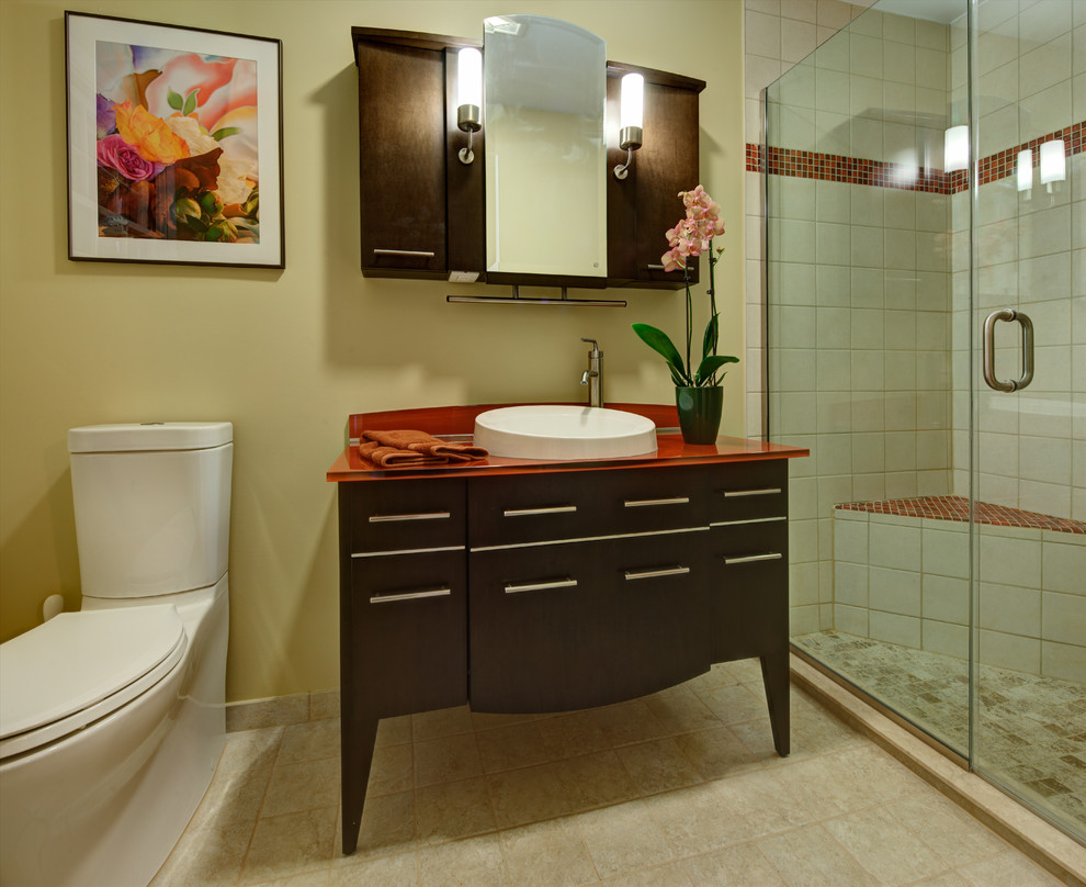 This is an example of a small traditional shower room bathroom in Atlanta with a vessel sink, freestanding cabinets, dark wood cabinets, glass worktops, an alcove shower, a two-piece toilet, beige tiles, ceramic tiles, beige walls and ceramic flooring.
