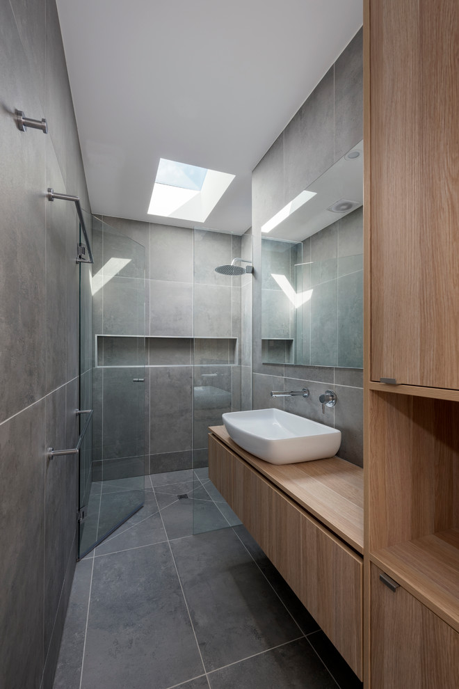 Photo of a contemporary shower room bathroom in Melbourne with flat-panel cabinets, light wood cabinets, an alcove shower, grey tiles, porcelain tiles, grey walls, porcelain flooring, a vessel sink and laminate worktops.