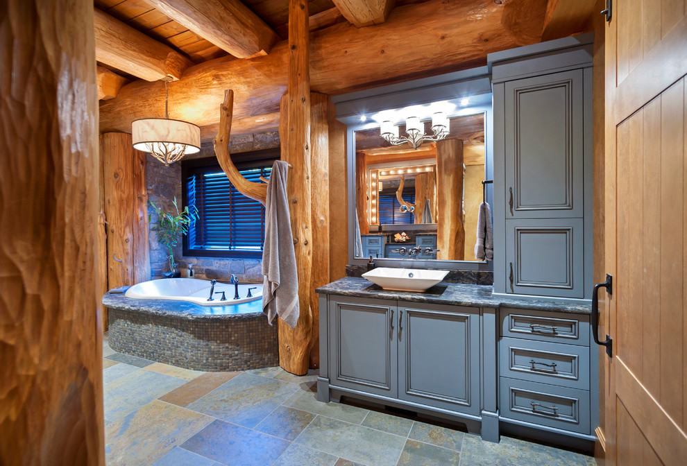 Modelo de cuarto de baño principal rústico grande con lavabo sobreencimera, armarios con paneles empotrados, puertas de armario azules, bañera encastrada, suelo gris y encimeras grises