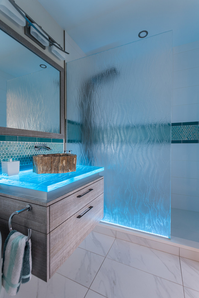 На фото: главная ванная комната среднего размера в стиле неоклассика (современная классика) с плоскими фасадами, серыми фасадами, угловой ванной, душем в нише, унитазом-моноблоком, синей плиткой, стеклянной плиткой, белыми стенами, полом из керамогранита, накладной раковиной, стеклянной столешницей, белым полом и душем с распашными дверями с