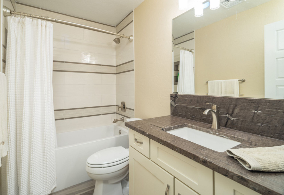 Klassisk inredning av ett mellanstort brun brunt badrum med dusch, med skåp i shakerstil, vita skåp, ett badkar i en alkov, en dusch/badkar-kombination, en toalettstol med separat cisternkåpa, beige kakel, vit kakel, porslinskakel, beige väggar, ett undermonterad handfat, brunt golv, dusch med duschdraperi, bänkskiva i täljsten och laminatgolv
