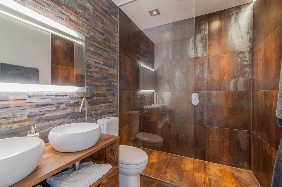 Small trendy master brown tile and stone tile porcelain tile doorless shower photo in Surrey with a console sink, open cabinets, medium tone wood cabinets, wood countertops, a one-piece toilet and gray walls