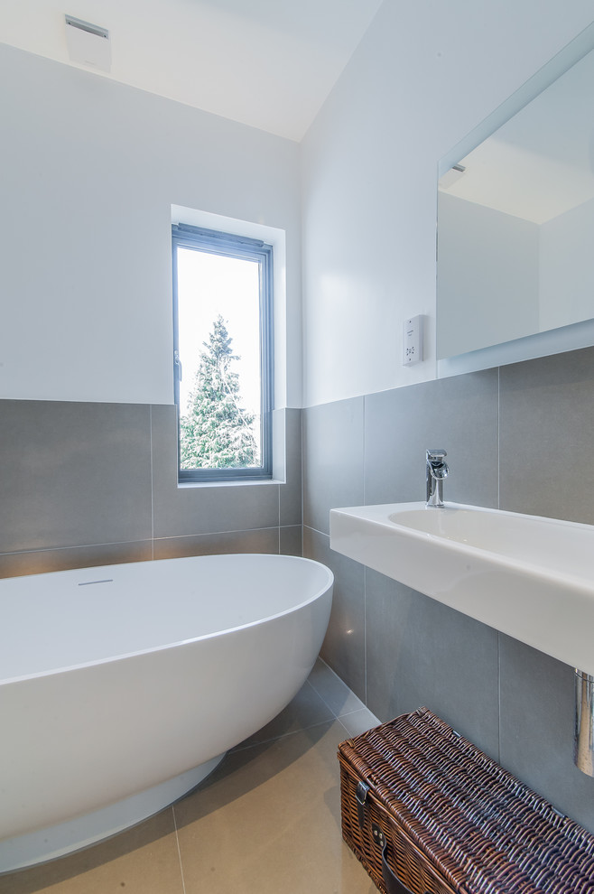 This is an example of a small contemporary family bathroom in Surrey with a wall-mounted sink, open cabinets, white cabinets, a freestanding bath, a walk-in shower, a one-piece toilet, grey tiles, porcelain tiles, grey walls and porcelain flooring.