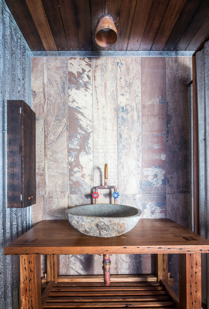 Inredning av ett industriellt mellanstort brun brunt en-suite badrum, med öppna hyllor, ett fristående badkar, en öppen dusch, en toalettstol med separat cisternkåpa, betonggolv, ett fristående handfat och träbänkskiva