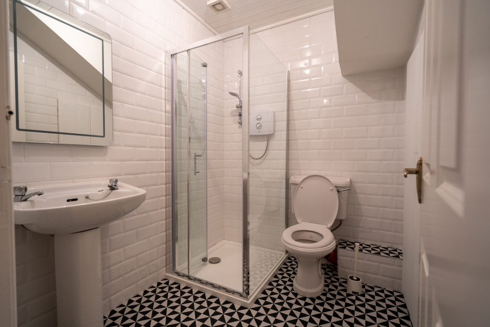 Стильный дизайн: маленькая ванная комната в классическом стиле с стеклянными фасадами, угловым душем, унитазом-моноблоком, белой плиткой, керамической плиткой, белыми стенами, полом из ламината, душевой кабиной, консольной раковиной, черным полом, душем с распашными дверями, тумбой под одну раковину и подвесной тумбой для на участке и в саду - последний тренд
