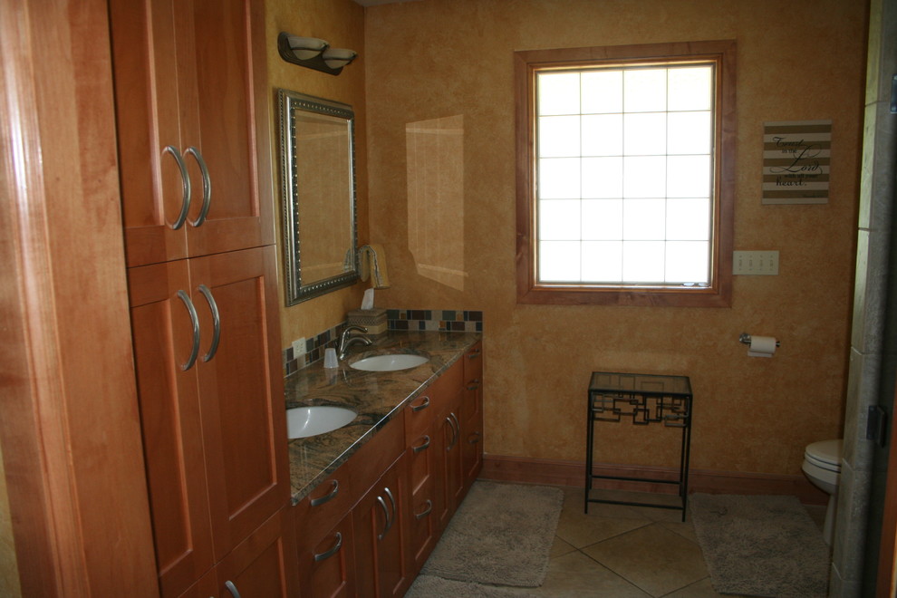 Cette photo montre une salle de bain principale craftsman en bois brun de taille moyenne avec un placard avec porte à panneau encastré, un carrelage beige, des carreaux de céramique, un sol en carrelage de céramique, un lavabo encastré, un plan de toilette en granite, un mur orange et un sol beige.
