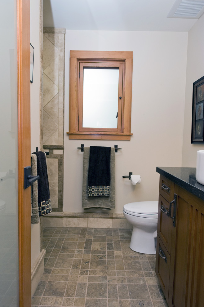 Modelo de cuarto de baño único y a medida clásico pequeño con armarios estilo shaker, puertas de armario de madera oscura, sanitario de dos piezas, paredes blancas, aseo y ducha, lavabo sobreencimera, suelo beige y encimeras negras