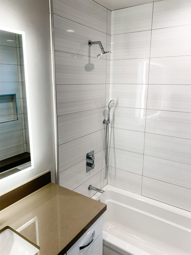 Skandinavisk inredning av ett litet beige beige badrum, med släta luckor, vita skåp, ett badkar i en alkov, en dusch/badkar-kombination, en toalettstol med hel cisternkåpa, vit kakel, porslinskakel, grå väggar, klinkergolv i porslin, ett undermonterad handfat, bänkskiva i kvarts, beiget golv och dusch med duschdraperi