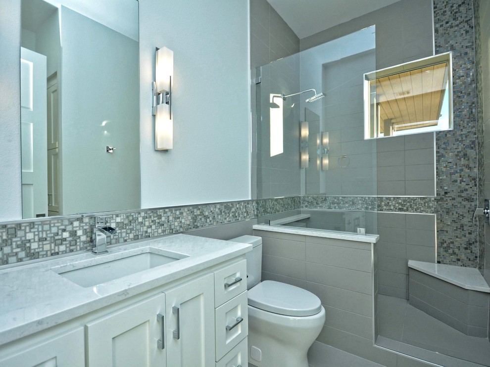 Aménagement d'une grande salle de bain contemporaine avec un placard avec porte à panneau surélevé, des portes de placard blanches, une douche d'angle, un carrelage gris, un mur blanc et un lavabo encastré.