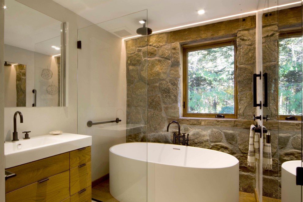 Cette photo montre une salle de bain principale montagne en bois clair avec un placard à porte plane, une baignoire indépendante, un combiné douche/baignoire, un mur beige, un lavabo intégré, aucune cabine et un mur en pierre.