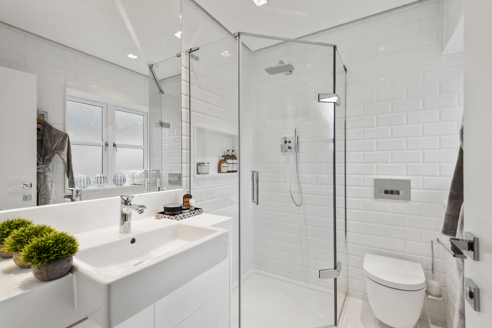 Inspiration for a large contemporary shower room bathroom in West Midlands with white cabinets, a corner shower, a wall mounted toilet, white tiles, white walls, white worktops, flat-panel cabinets, metro tiles, white floors and a hinged door.