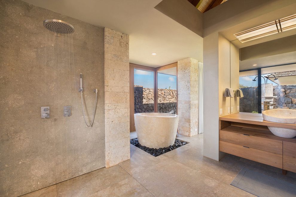 Exotisk inredning av ett en-suite badrum, med skåp i mellenmörkt trä, ett fristående badkar, en öppen dusch, en bidé, grå väggar, kalkstensgolv, ett fristående handfat, träbänkskiva, grått golv och med dusch som är öppen