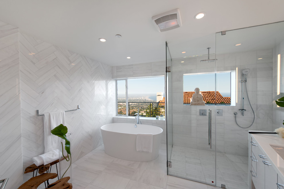 Modern inredning av ett mellanstort vit vitt en-suite badrum, med släta luckor, vita skåp, ett fristående badkar, en kantlös dusch, en vägghängd toalettstol, vit kakel, marmorkakel, vita väggar, marmorgolv, ett undermonterad handfat, marmorbänkskiva, vitt golv och dusch med gångjärnsdörr