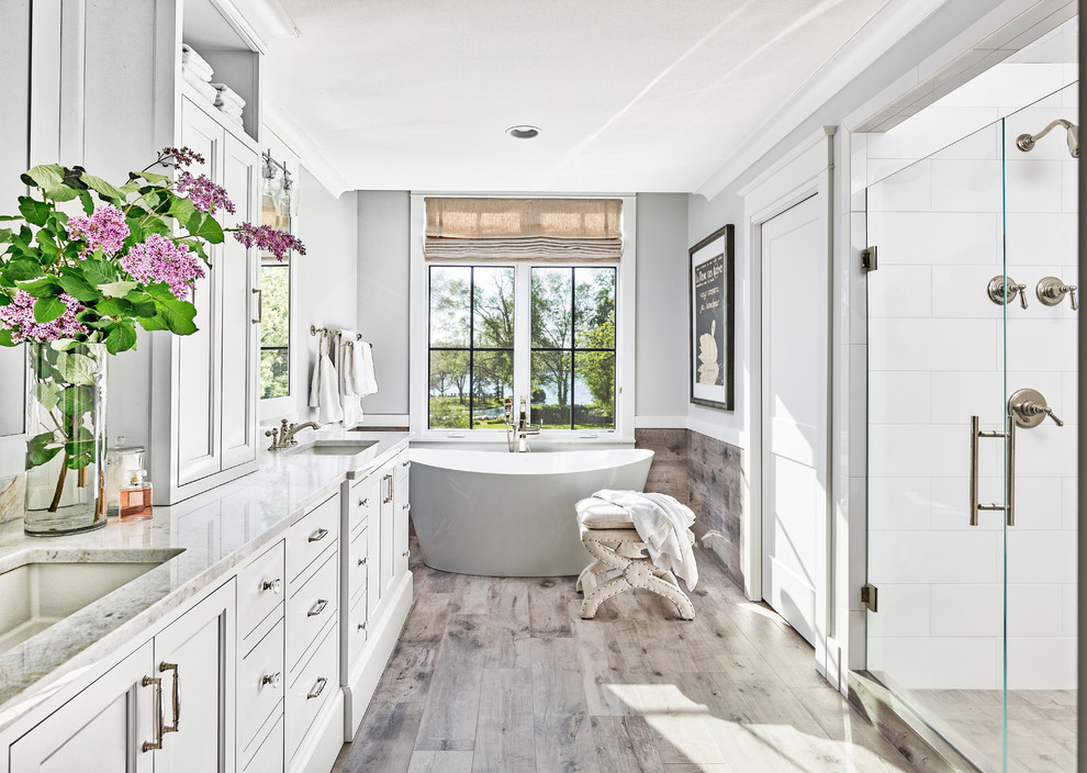 Idéer för att renovera ett stort maritimt vit vitt en-suite badrum, med vita skåp, ett fristående badkar, en dusch i en alkov, vit kakel, grå väggar, klinkergolv i porslin, marmorbänkskiva, brunt golv, dusch med gångjärnsdörr och ett undermonterad handfat