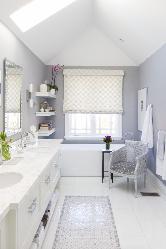Imagen de cuarto de baño clásico renovado con lavabo bajoencimera, puertas de armario blancas, encimera de mármol, bañera exenta, baldosas y/o azulejos blancos y paredes púrpuras