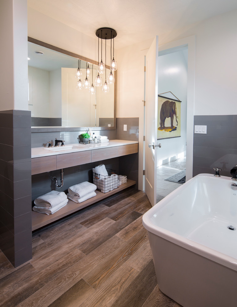 Modern inredning av ett en-suite badrum, med ett fristående badkar, grå kakel, glaskakel, vita väggar, klinkergolv i keramik, ett undermonterad handfat, bänkskiva i kvarts, släta luckor och skåp i ljust trä