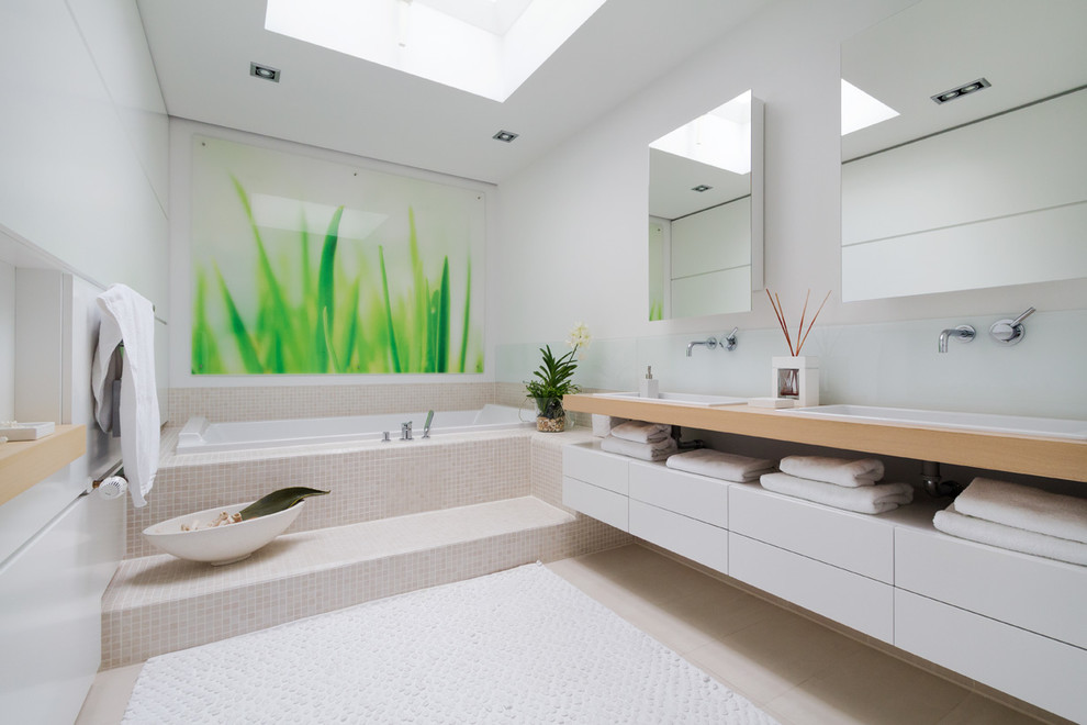 Example of a large trendy mosaic tile and beige tile drop-in bathtub design in Hamburg with flat-panel cabinets, white cabinets, white walls, a drop-in sink, wood countertops and brown countertops