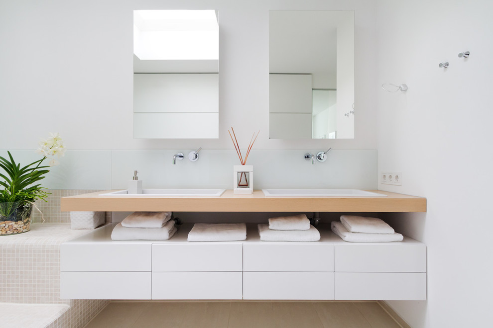 Modernes Badezimmer mit flächenbündigen Schrankfronten, weißen Schränken, weißer Wandfarbe, Einbauwaschbecken, Einbaubadewanne und Waschtisch aus Holz in Hamburg