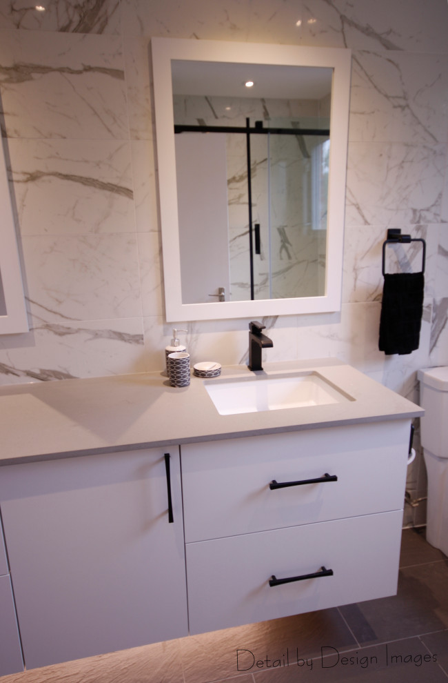 This is an example of a medium sized contemporary family bathroom in Ottawa with flat-panel cabinets, white cabinets, an alcove bath, a shower/bath combination, a one-piece toilet, black and white tiles, porcelain tiles, white walls, porcelain flooring, a submerged sink, engineered stone worktops, grey floors, a sliding door, grey worktops, a single sink and a floating vanity unit.