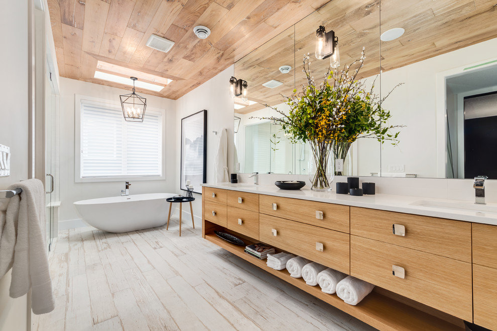 Inspiration for a large contemporary ensuite bathroom in Calgary with flat-panel cabinets, light wood cabinets, a freestanding bath, white walls, engineered stone worktops, white floors, an alcove shower, light hardwood flooring, a submerged sink and a hinged door.