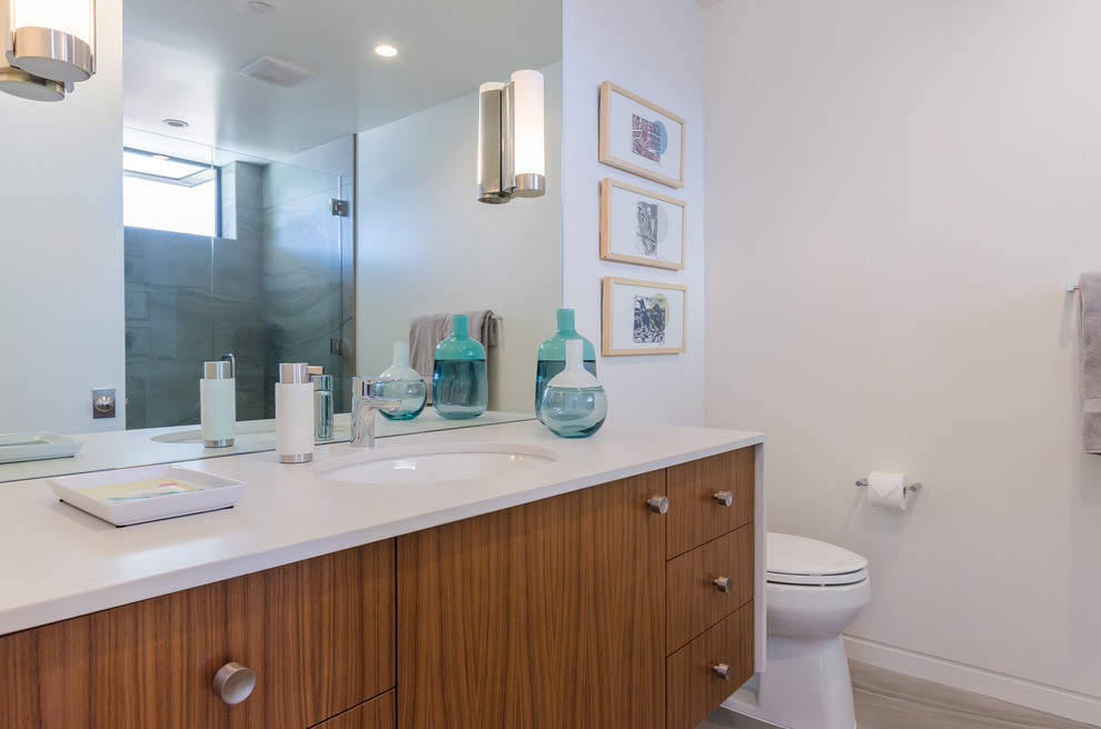 This is an example of a small contemporary shower room bathroom in San Francisco with flat-panel cabinets, light wood cabinets, an alcove shower, a two-piece toilet, white tiles, white walls, travertine flooring, a submerged sink, solid surface worktops, beige floors and a hinged door.