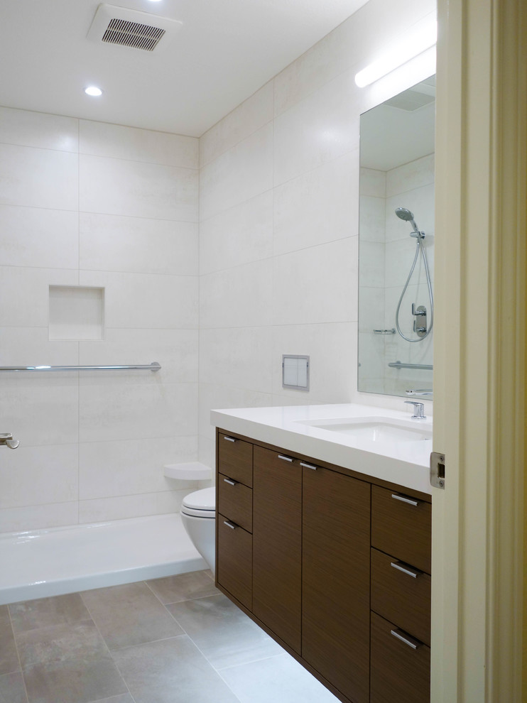 Inspiration for a medium sized modern shower room bathroom in San Francisco with flat-panel cabinets, brown cabinets, an alcove shower, a wall mounted toilet, beige tiles, porcelain tiles, white walls, porcelain flooring, a submerged sink, engineered stone worktops, beige floors, a sliding door and white worktops.