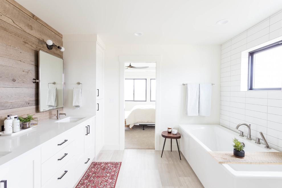 Foto på ett lantligt vit badrum, med skåp i shakerstil, vita skåp, ett hörnbadkar, vit kakel, vita väggar, ett undermonterad handfat och grått golv