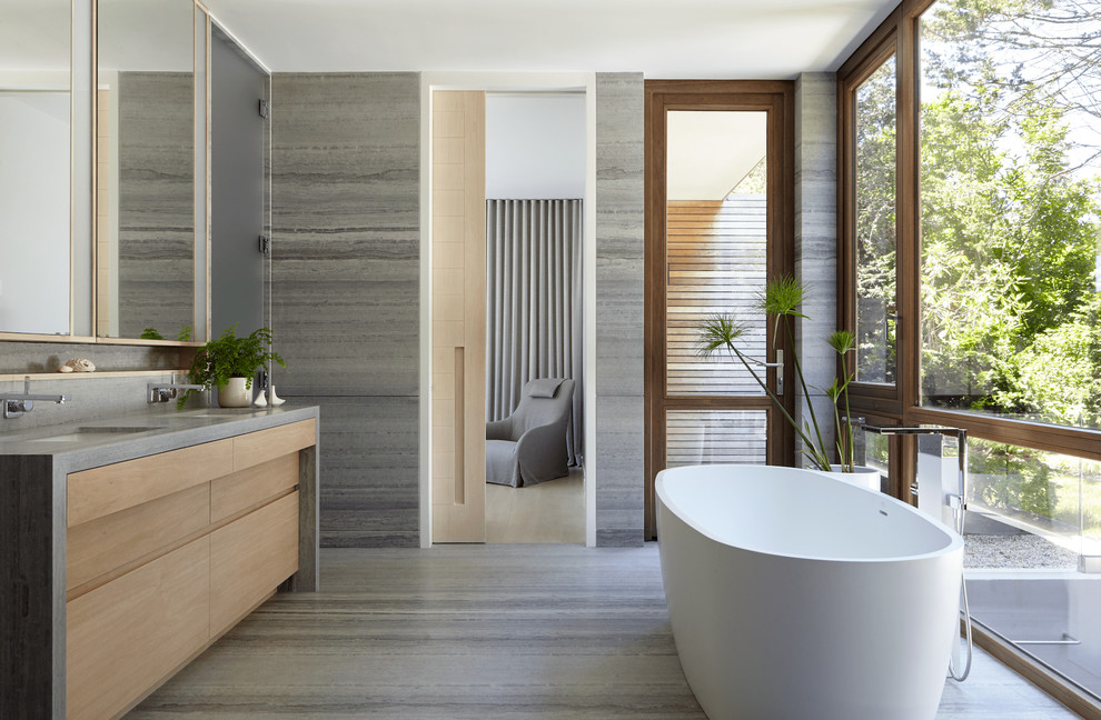 На фото: главная ванная комната в морском стиле с серой плиткой, серым полом, серой столешницей, плоскими фасадами, светлыми деревянными фасадами, отдельно стоящей ванной, серыми стенами и врезной раковиной
