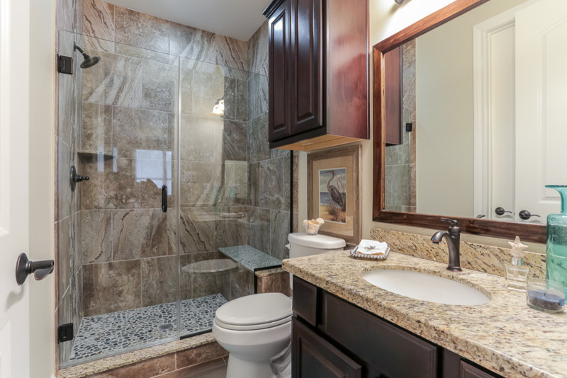 Inspiration for a small coastal shower room bathroom in Houston with a submerged sink, raised-panel cabinets, dark wood cabinets, granite worktops, an alcove shower, a one-piece toilet, brown tiles, stone tiles, beige walls and porcelain flooring.