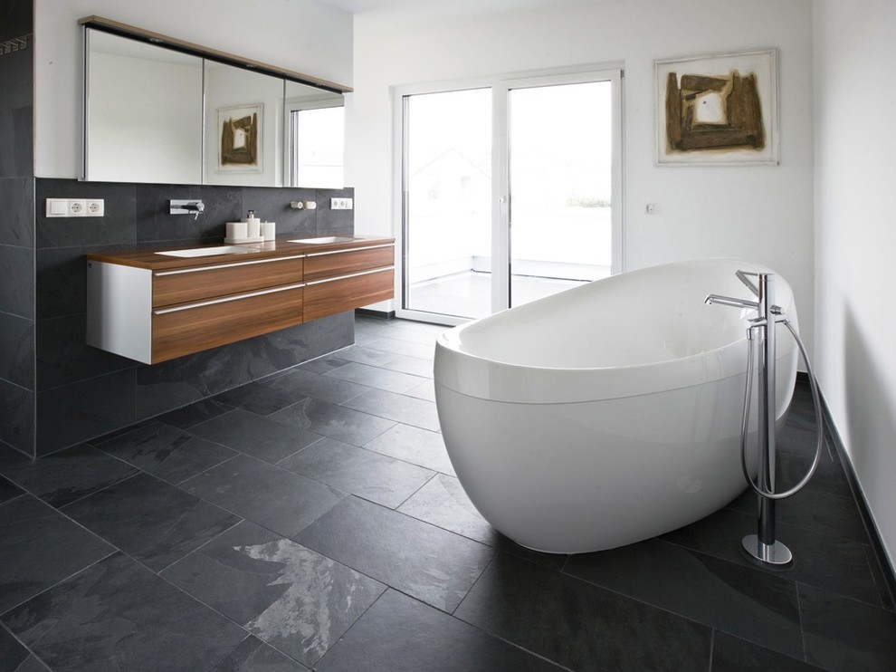 Exempel på ett stort modernt en-suite badrum, med svart kakel, keramikplattor, släta luckor, skåp i mellenmörkt trä, ett fristående badkar, vita väggar, skiffergolv, ett undermonterad handfat och träbänkskiva