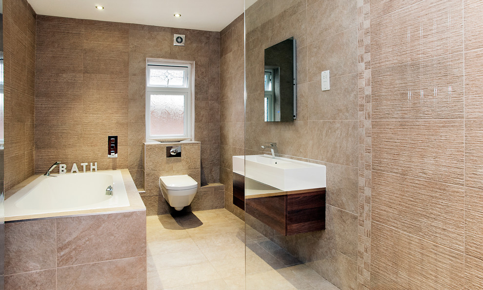 Foto på ett stort funkis badrum för barn, med ett väggmonterat handfat, ett hörnbadkar, en öppen dusch, en vägghängd toalettstol, beige kakel, stenkakel, beige väggar och klinkergolv i keramik