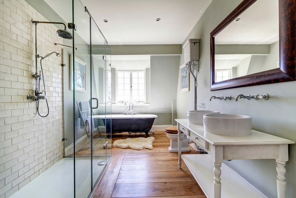 На фото: ванная комната в классическом стиле с белыми фасадами, ванной на ножках, двойным душем, раздельным унитазом, серыми стенами, паркетным полом среднего тона и настольной раковиной с